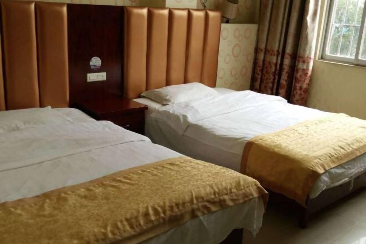 Una habitación de hotel con dos camas individuales, un cabecero de madera, una mesita de noche y una ventana con cortinas.