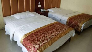 Een hotelkamer met twee bedden, elk voorzien van witte lakens en een bruin hoofdeinde. Tussen de bedden staat een nachtkastje met een telefoon en een klein tafeltje.