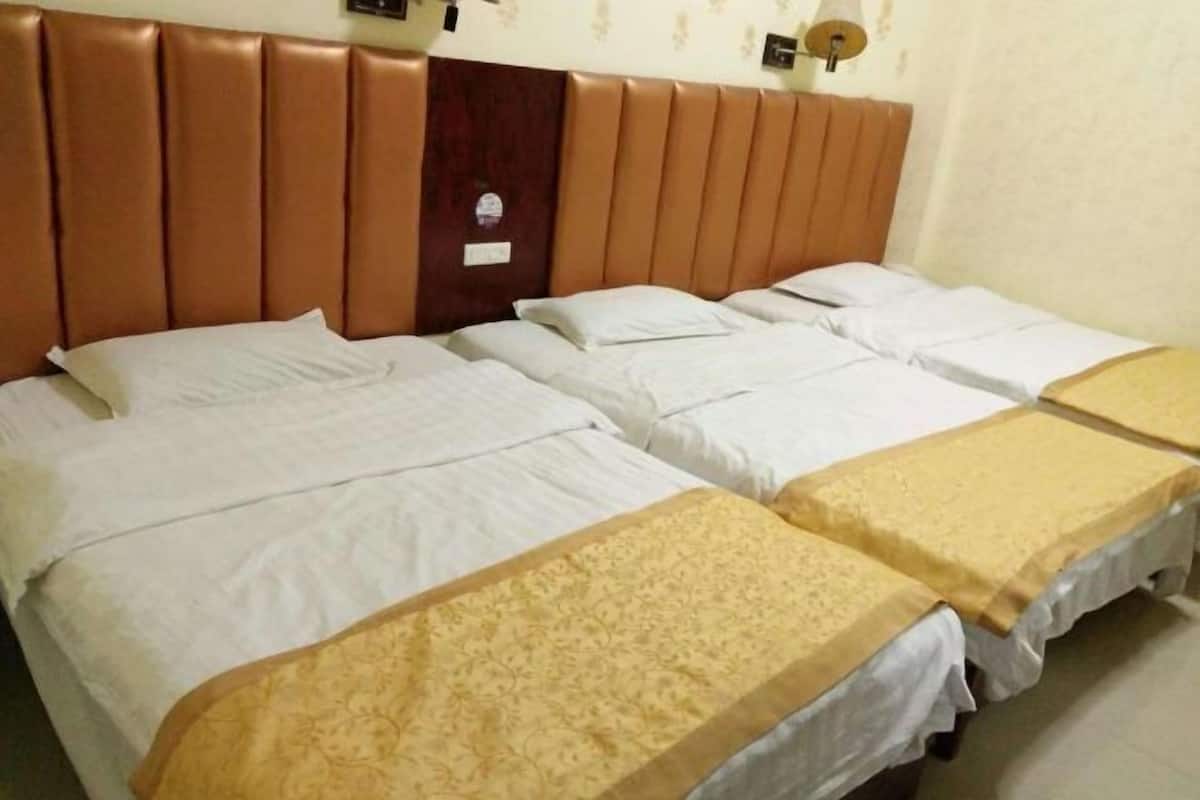 Una habitación de hotel con un cabecero acolchado marrón, tres camas con ropa blanca y un corredor decorativo amarillo sobre las camas.