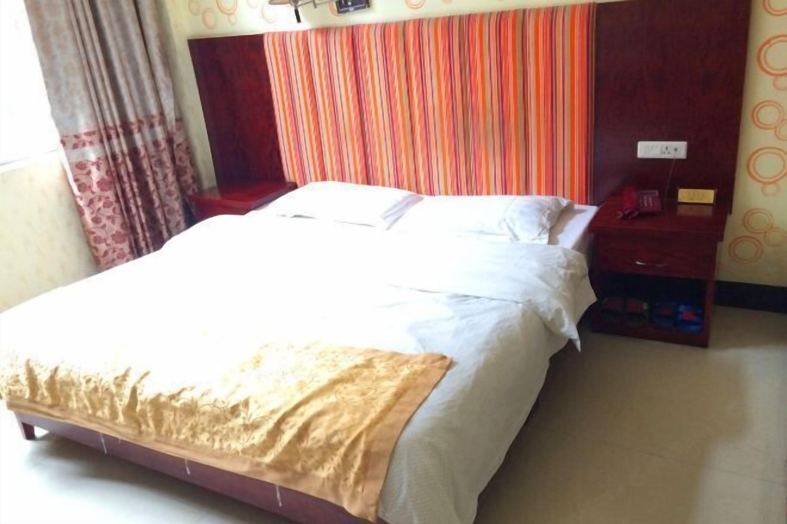 Una habitación de hotel con cama, mesita de noche, teléfono rojo y un enchufe en la pared.