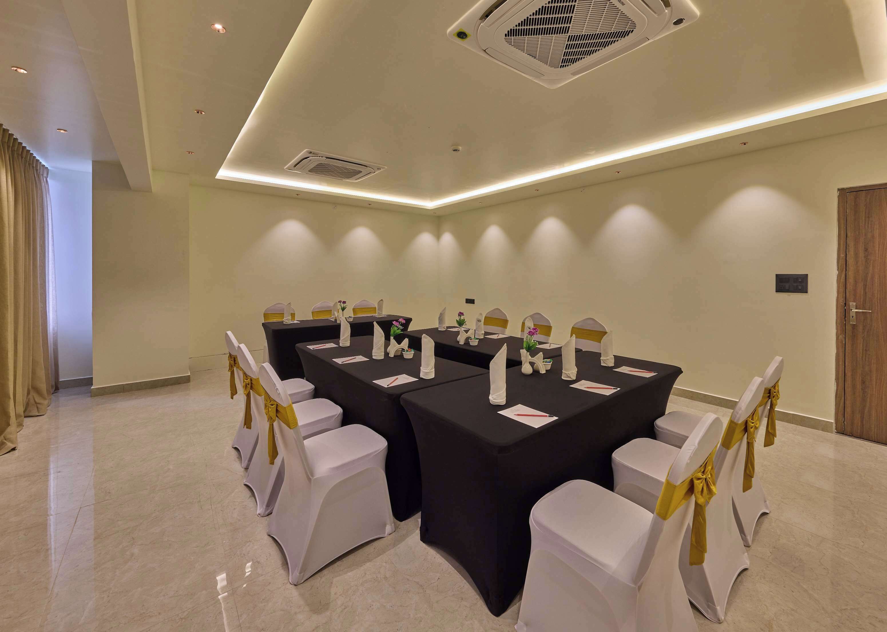 A conference room with a large table, white chairs with yellow sashes, and a ceiling vent.