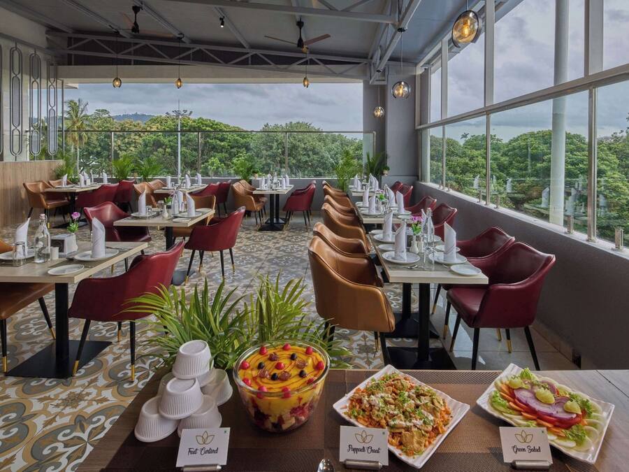 A restaurant with tables set for dining, a large window offering a view of greenery, and a ceiling fan.
