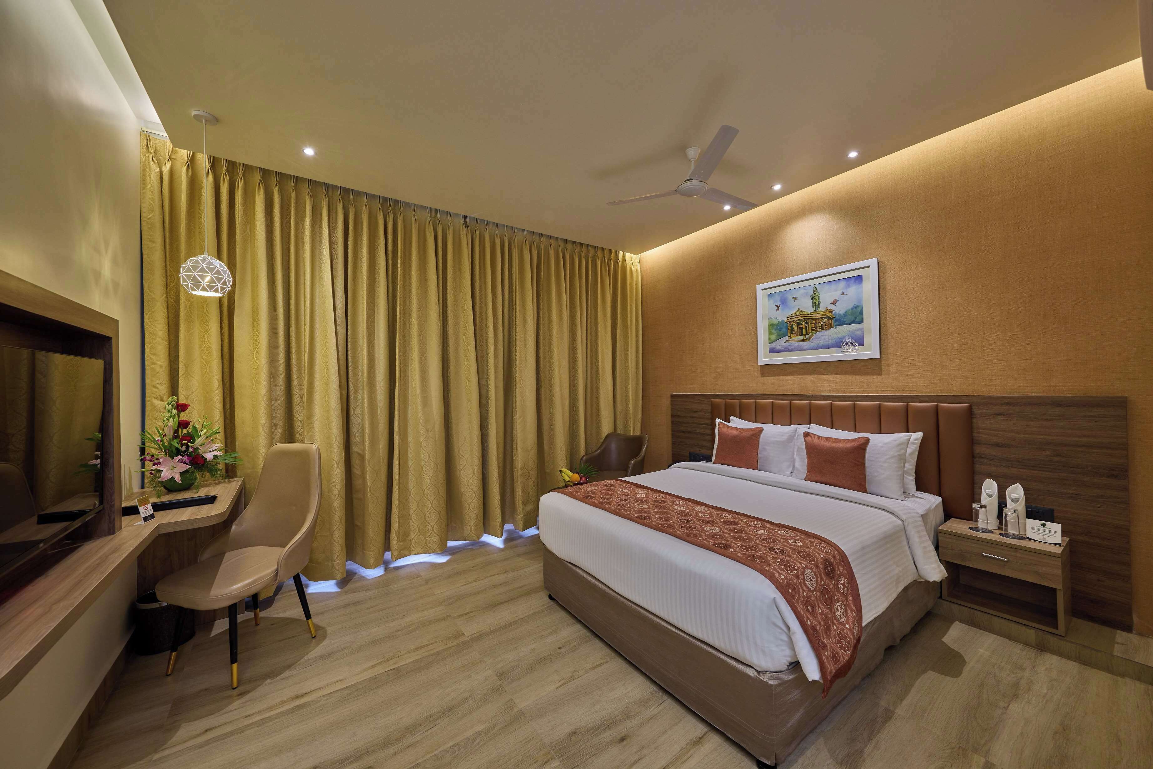 Habitación de hotel con una cama grande, un escritorio con silla, un televisor, un ventilador de techo y un cuadro en la pared.