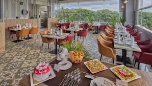 Un restaurante con varias mesas y sillas, una variedad de platos en las mesas, y vistas al exterior con vegetación.
