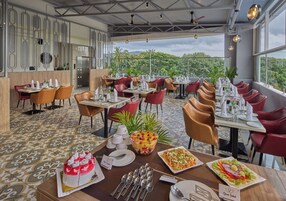 Un restaurant doté de nombreuses tables et chaises, où l’on peut trouver une variété de plats sur les tables, et qui offre une vue sur la verdure environnante.