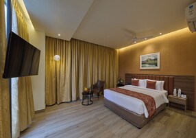 A hotel room with a large bed, a flat-screen TV, a desk with a chair, and a painting on the wall.