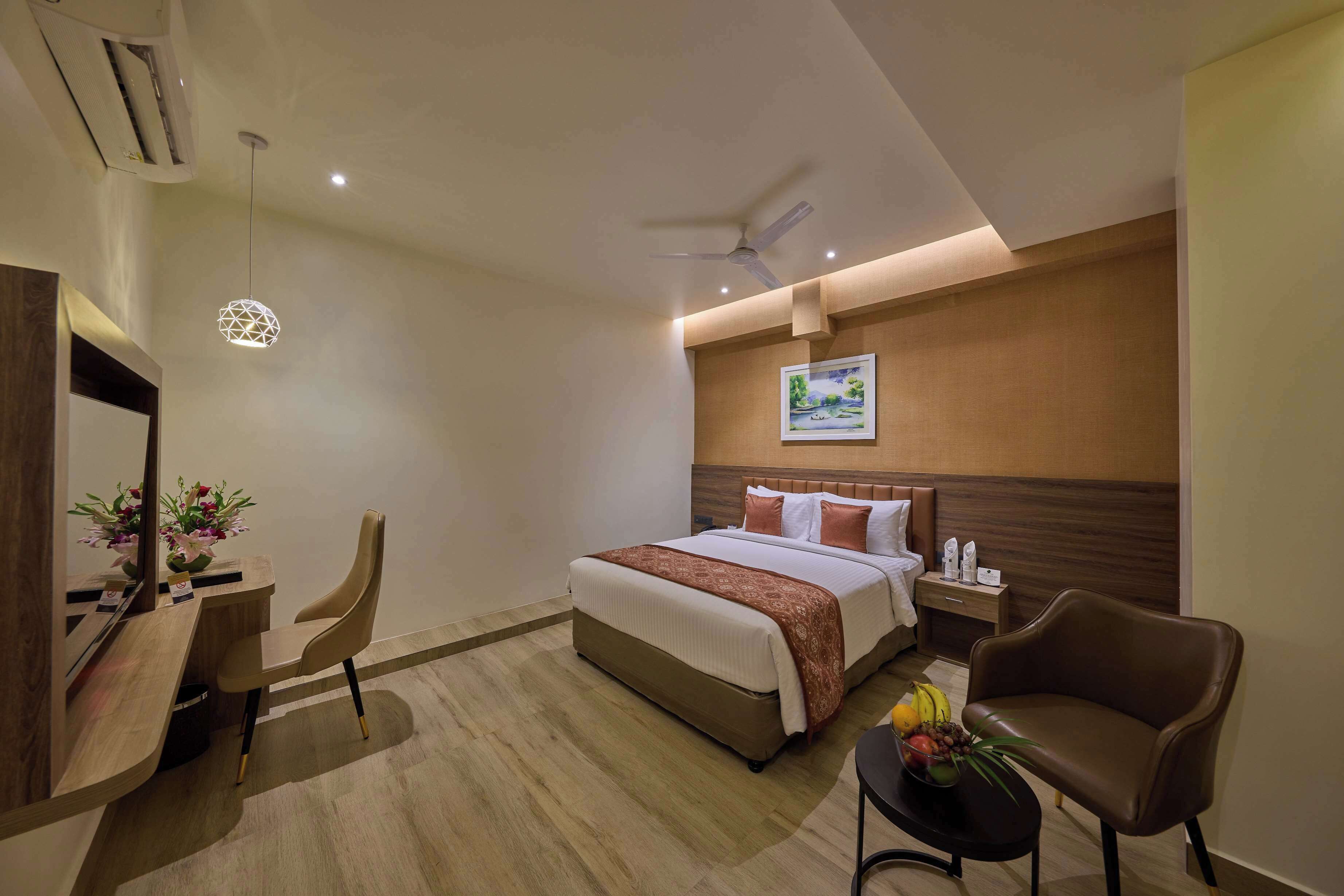 A hotel room with a bed, desk, chair, and a small table with fruits.