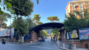 A gated entrance with a covered walkway, a brick wall, and a building with large windows in the background. - F.ROOMS NAPOLI VIA SEMENTINI (Naples)