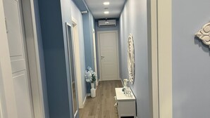 A hallway with blue walls, wooden flooring, and white doors. There is a small table with a vase and a decorative item on it. - F.ROOMS NAPOLI VIA SEMENTINI (Naples)