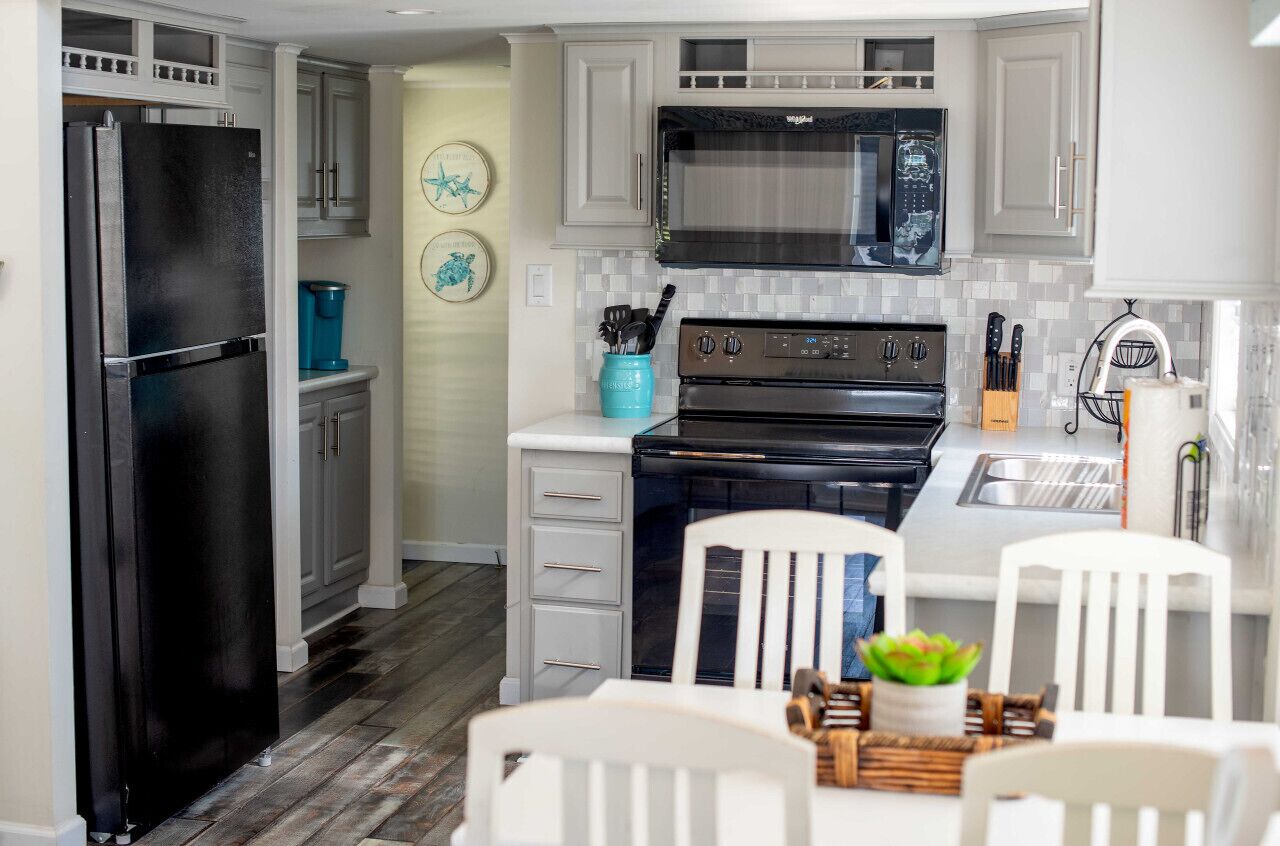 A modern kitchen with white cabinets, a black refrigerator, a stove, and a microwave. There is a sink and a window above the sink.