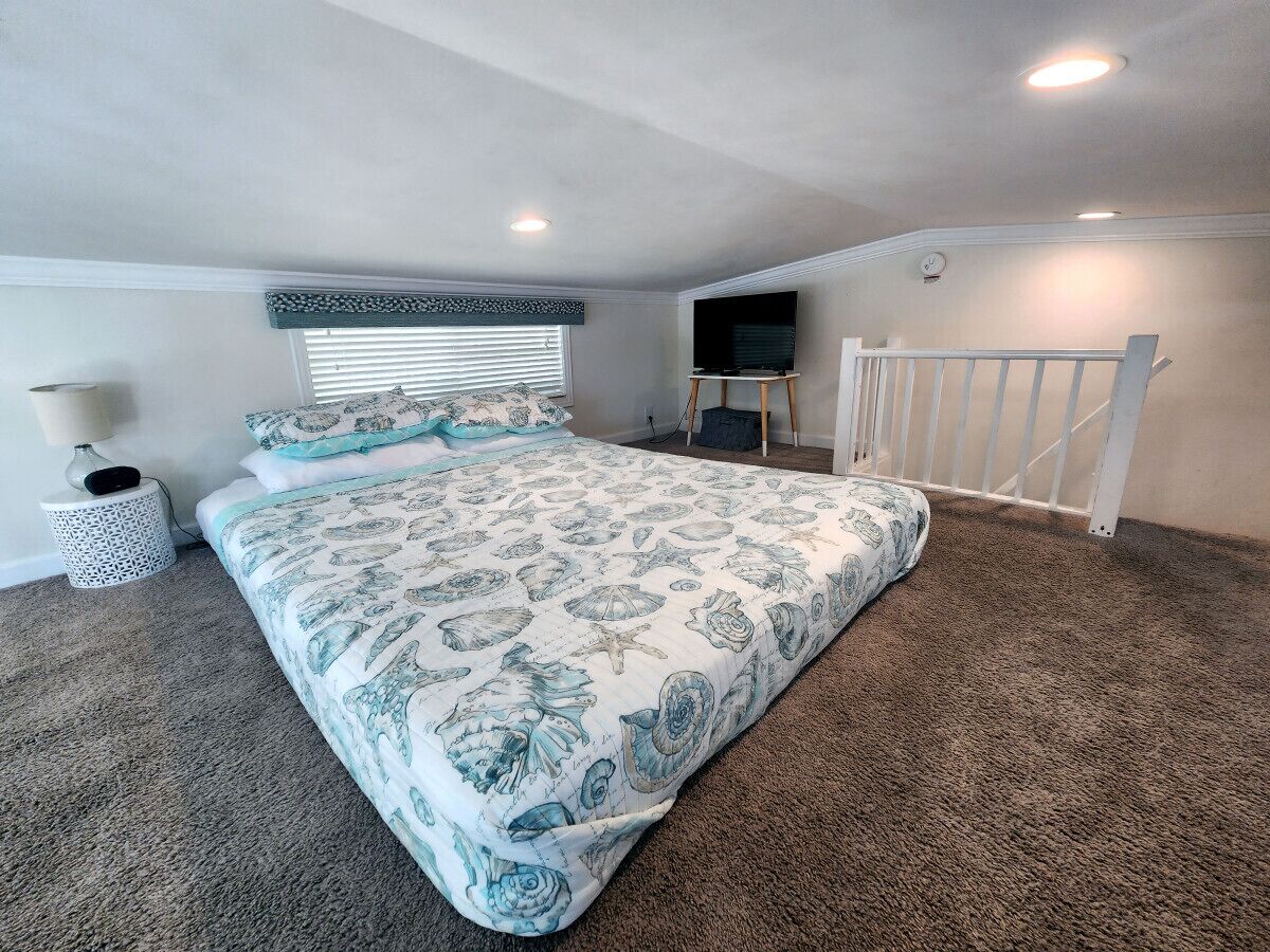 A bedroom with a large bed, a TV mounted on the wall, and a staircase leading to an upper level.