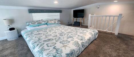 A bedroom with a large bed, a TV mounted on the wall, and a staircase leading to an upper level.