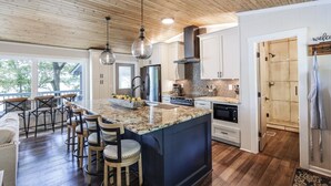 A modern kitchen with a large island, wooden ceiling, and bar seating area. - The Overlook at Langford - Private dock with SUPs, Kayaks, and Ping Pong (Leesville)
