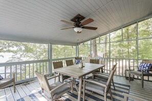 A covered outdoor seating area with a table and chairs, large windows, and a ceiling fan. - The Overlook at Langford - Private dock with SUPs, Kayaks, and Ping Pong (Leesville)