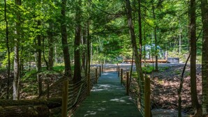 A wooden suspension bridge in a forested area with a pathway leading to a building. - Allure Muskoka Glass Dome (Huntsville)