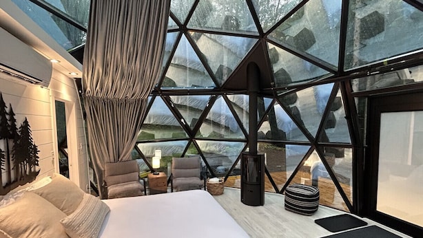 A modern bedroom with a large bed, a seating area, and a fireplace. - Allure Muskoka Glass Dome (Huntsville)