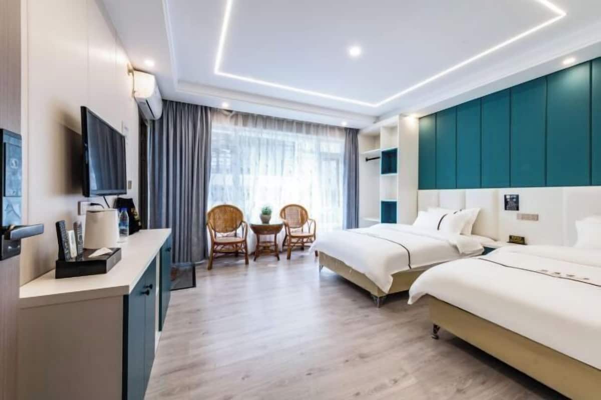 Une chambre d’hôtel moderne dotée d’un grand lit, d’un bureau avec une télévision, de deux fauteuils en osier et d’une grande fenêtre avec des rideaux.