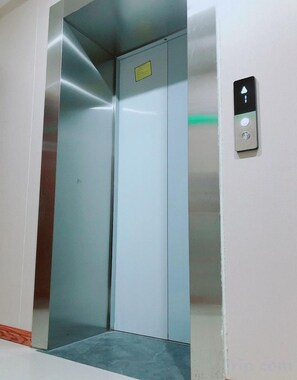 An elevator with a control panel on the wall, a door with a yellow sign, and a metal step at the bottom. - Fuxian Lake Jinxiu Hotel (Lunchong Scenic Area) (Chengjiang)
