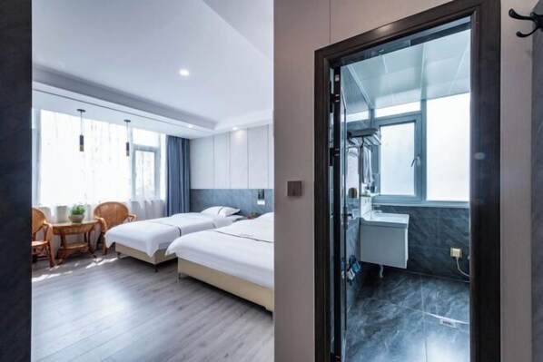 A modern hotel room with two beds, a sitting area with a table and chairs, a large window, and a bathroom with a glass partition. - Fuxian Lake Jinxiu Hotel (Lunchong Scenic Area) (Chengjiang)