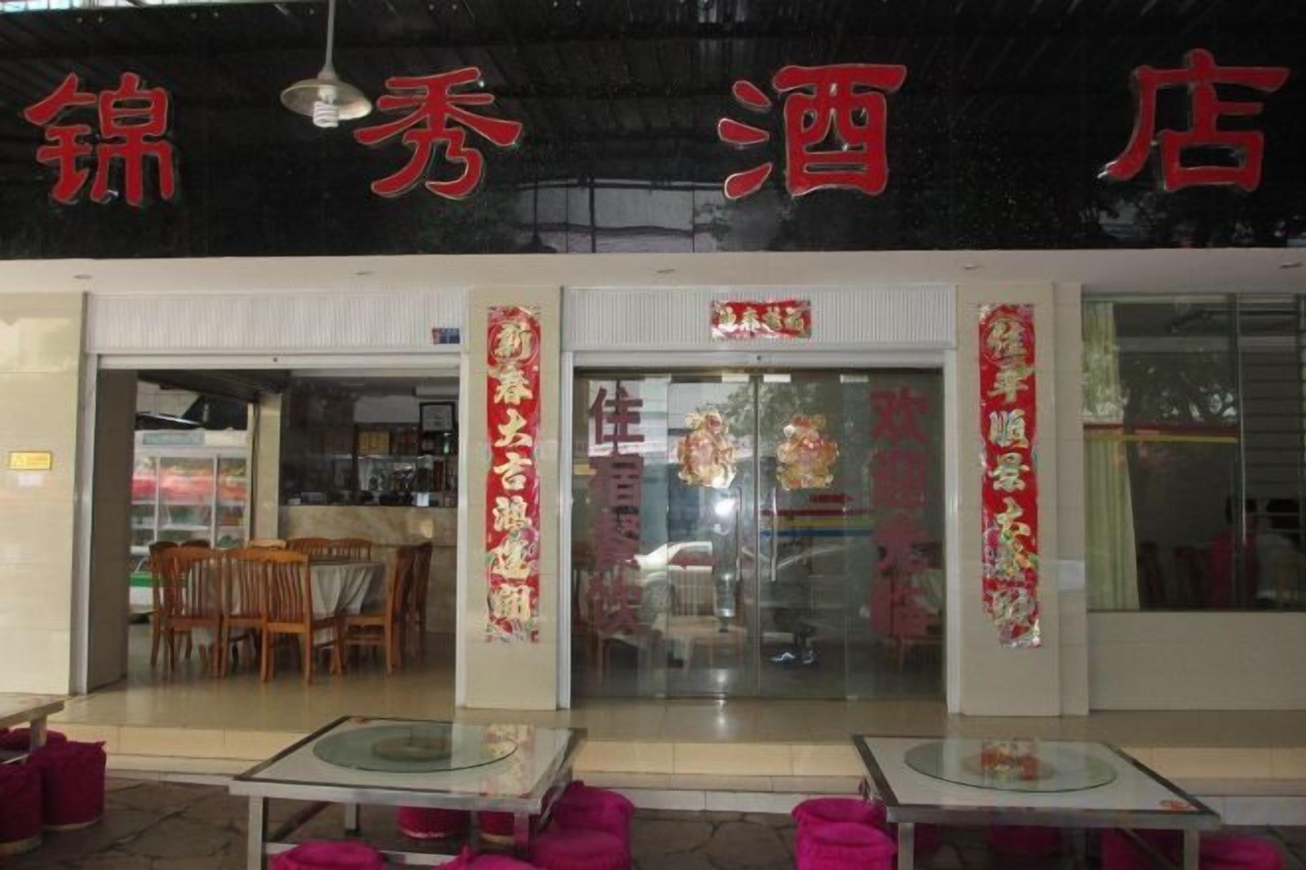 A restaurant with a glass entrance, tables with pink cushions, and red decorations.