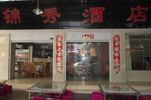 Restaurante com entrada de vidro, mesas com almofadas cor-de-rosa e decorações vermelhas.