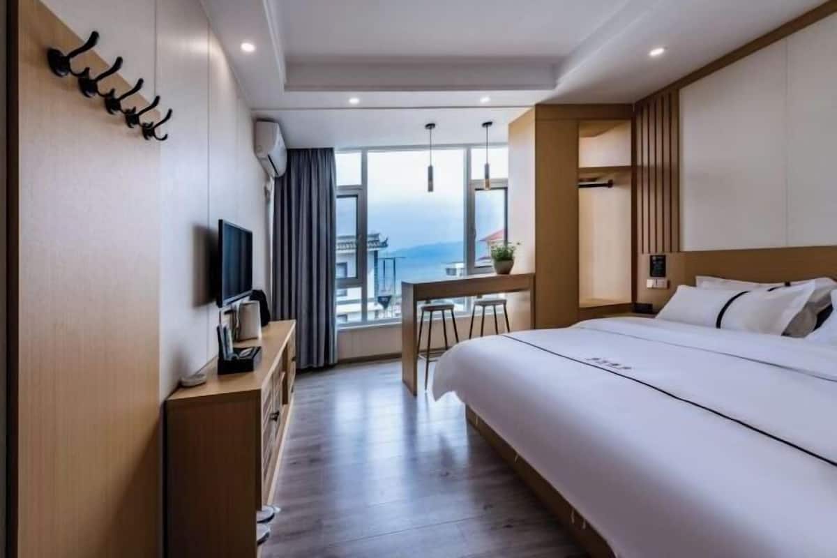 Une chambre d’hôtel moderne dotée d’un grand lit, d’un bureau avec une chaise, d’une télévision et offrant une vue sur la ville.