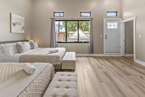 A bedroom with two beds, a bench, a window with a view, and a door.