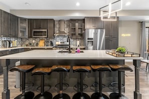 Une cuisine moderne avec des meubles de couleur sombre, un grand îlot central doté de tabourets, un réfrigérateur en acier inoxydable et un pare-feu décoratif.