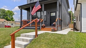 A two-story house with a front porch, a wooden staircase, and an American flag. - Indy Carriage House in Downtown (Indianapolis)