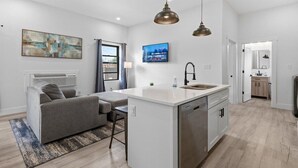 A modern living room with a gray sofa, a small dining table, and a kitchen area with a white countertop and stainless steel appliances. - Indy Carriage House in Downtown (Indianapolis)