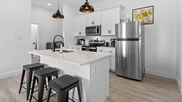A modern kitchen with white cabinetry, stainless steel appliances, and a central island with bar stools. - Indy Carriage House in Downtown (Indianapolis)