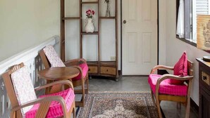 A room with a wooden chair and a table, a small shelf with a vase, and a door with a number plate. - The Sayla Hotel (Chiang Mai)