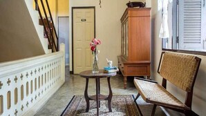 A hallway with a staircase, a wooden cabinet, a small table with a vase of flowers, and a wicker chair. - The Sayla Hotel (Chiang Mai)