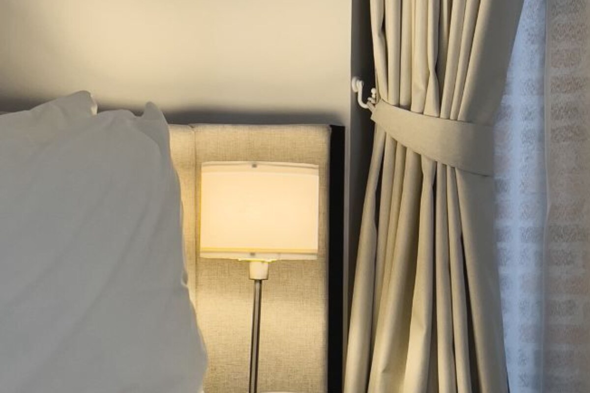 A hotel room with a bed, a bedside lamp, and curtains.
