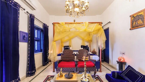 A room with a bed, a chandelier, a small table with a lamp, and a blue sofa. - Harpalsar Haveli Jaipur (Jaipur)