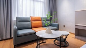 Una sala de estar moderna con un sofá gris, cojines naranjas, un jarrón blanco con una planta y una mesa redonda con dos sillas.