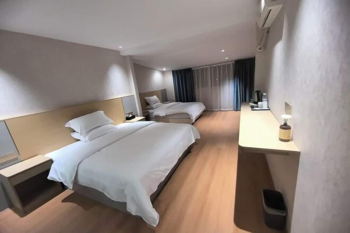 Una habitación de hotel moderna con dos camas, una mesita de noche, un escritorio con lámpara y un cesto de basura.