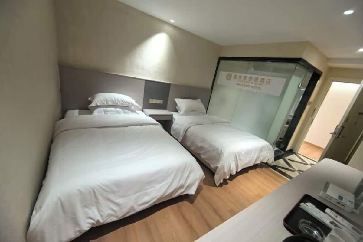 Habitación de hotel con dos camas, un escritorio y un separador de vidrio.