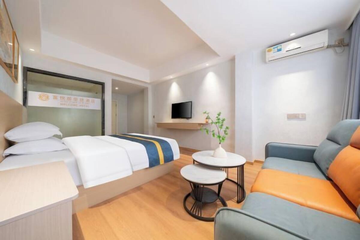 Habitación de hotel con cama, sofá, una mesita, televisor y aire acondicionado.