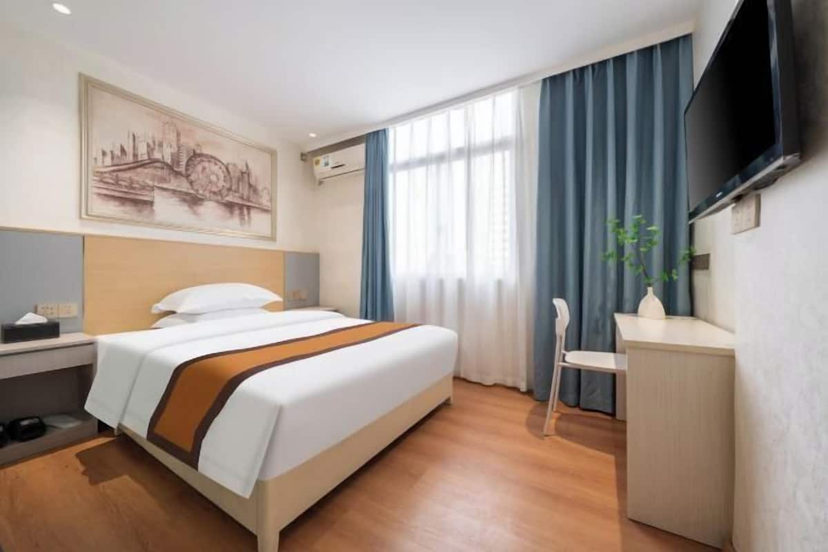 Habitación de hotel con cama, escritorio, silla, televisor y ventana con cortinas.