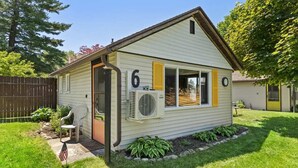 A single-story house with a number '6' on the side, a small porch with a chair, and an air conditioning unit mounted on the wall. - Chippewa Bluffs Resort - 2BR 2BA Cabins (Chippewa Lake)