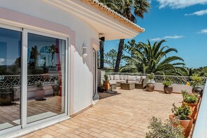 Una terraza en la azotea con un sofá, plantas en macetas y vistas a palmeras.