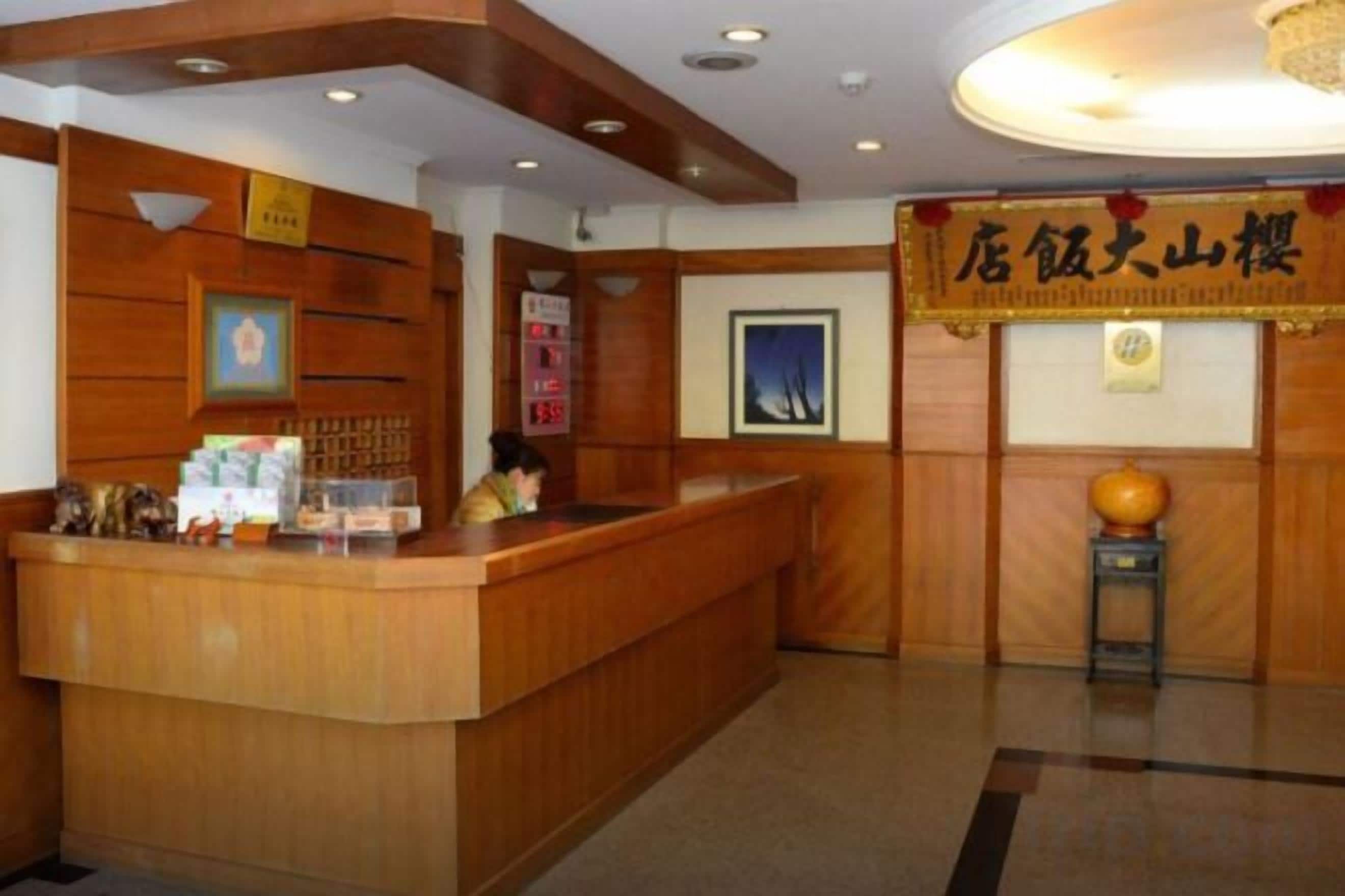 Een receptiebalie met een houten afwerking, een ingelijst schilderij erboven en een bord met Chinese karakters.