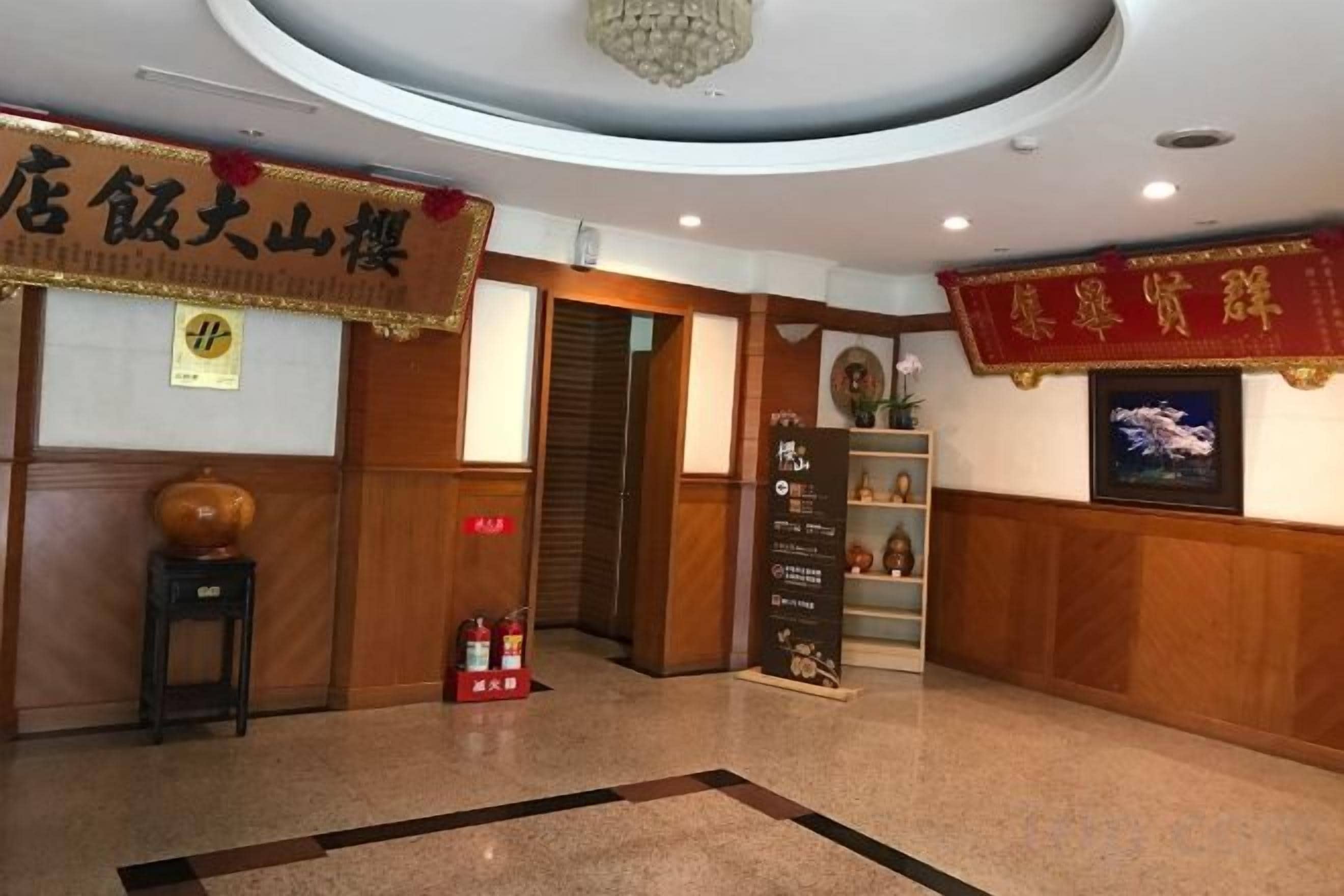 A hotel lobby with a reception desk, a chandelier, a red banner, and a wall-mounted television.