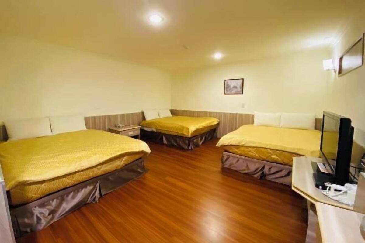 A hotel room with two beds, wooden flooring, a desk with a computer, and a framed picture on the wall.
