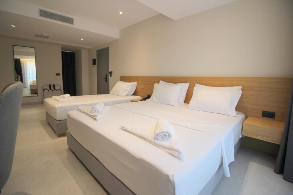 A hotel room with two beds, a wooden headboard, a small bedside table, and a large mirror.