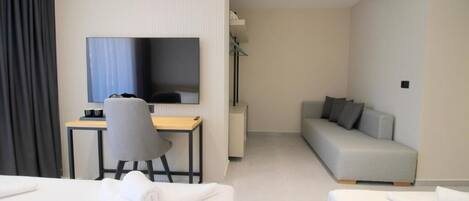 A modern hotel room with a bed, a desk with a chair, a sofa, and a TV.
