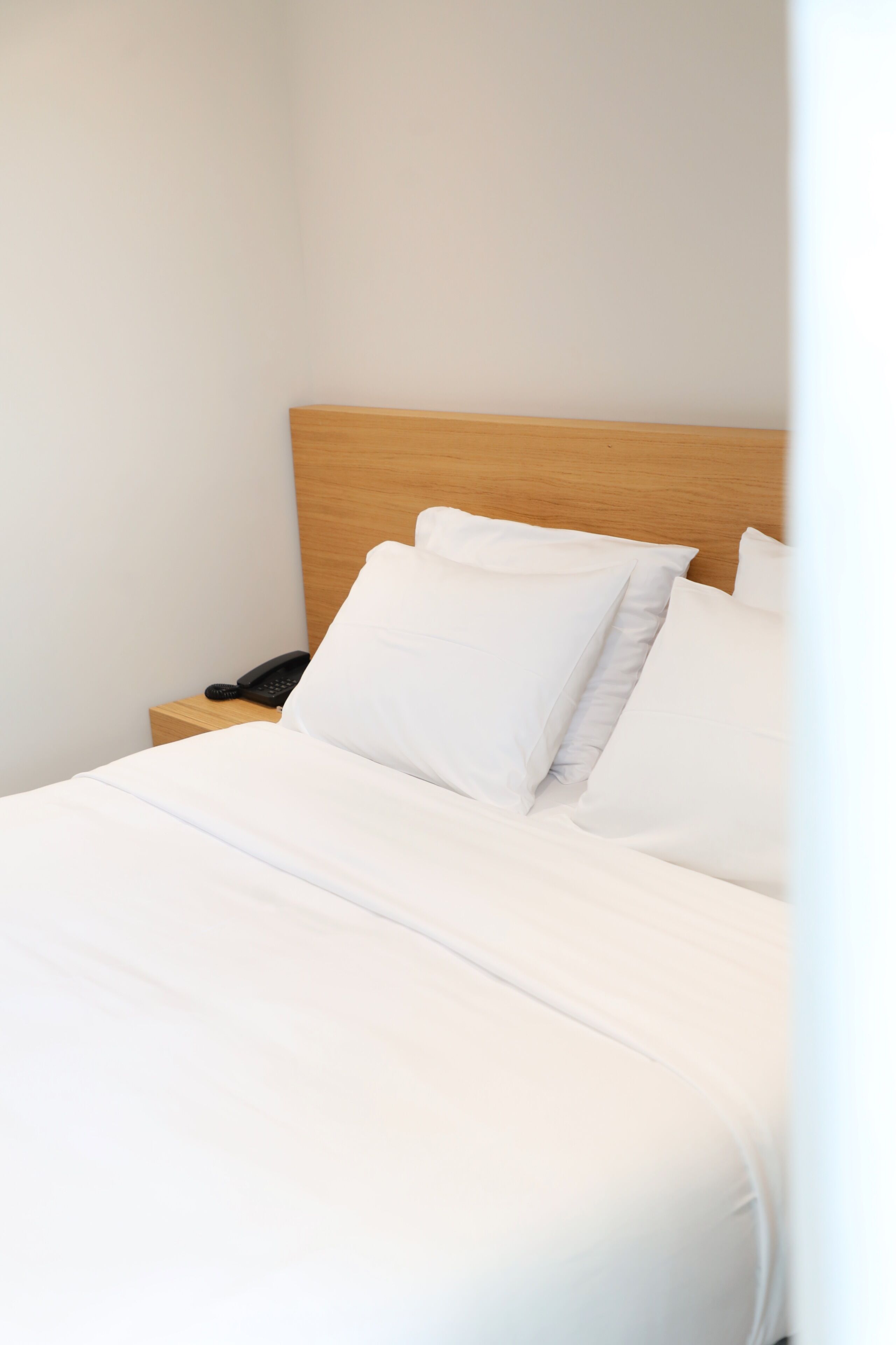 Una cama bien hecha con ropa blanca, un cabecero de madera y un teléfono en la mesita de noche.