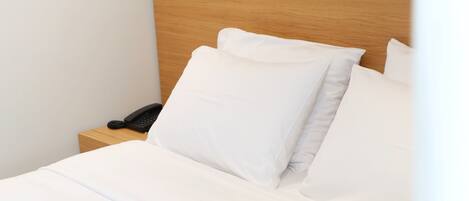 Una cama bien hecha con ropa blanca, un cabecero de madera y un teléfono en la mesita de noche.