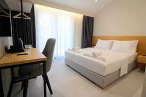 A hotel room with a bed, a desk, a chair, a bedside table, and a TV.